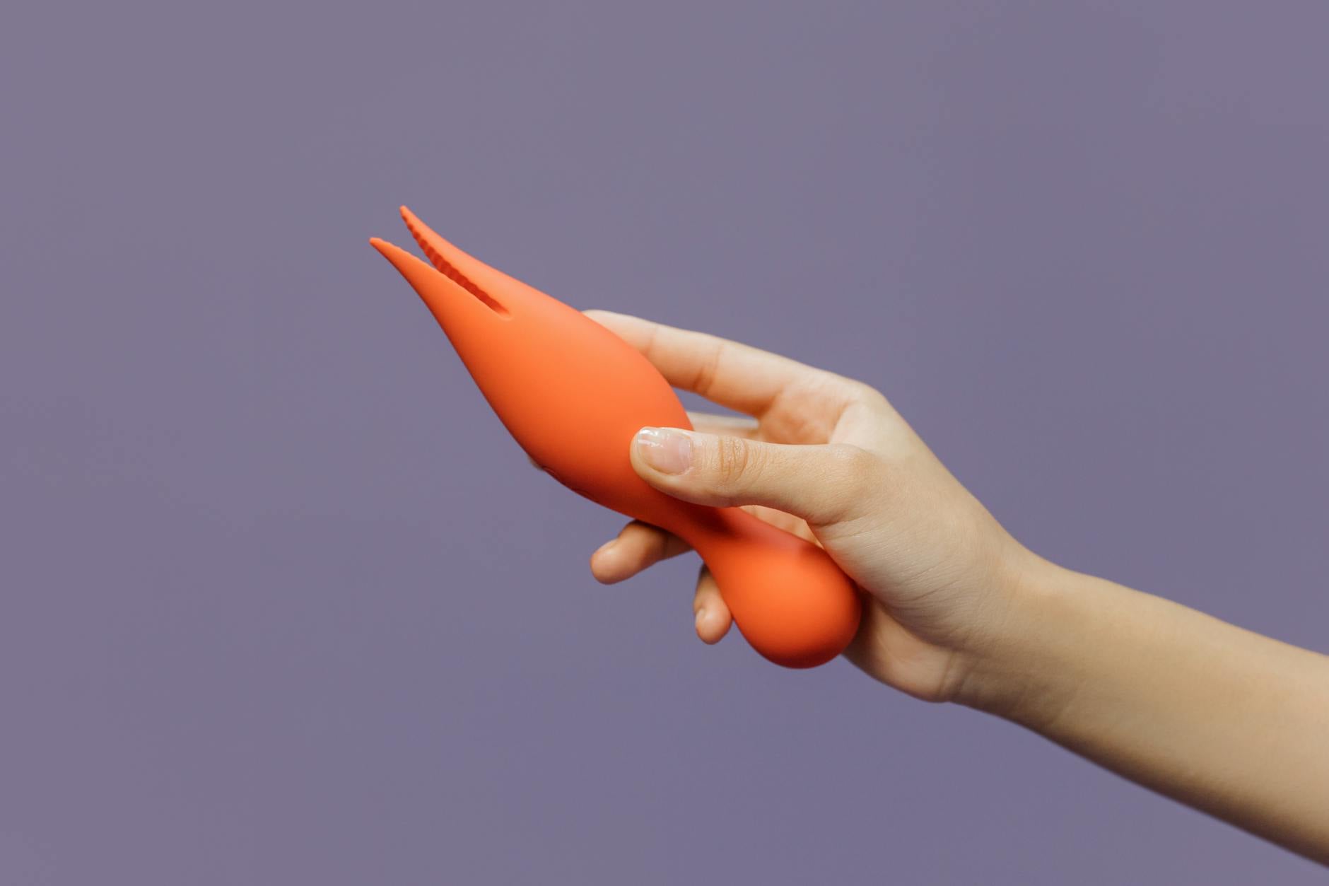 Frau hält orangefarbenen Vibrator vor minimalistische lila Kulisse